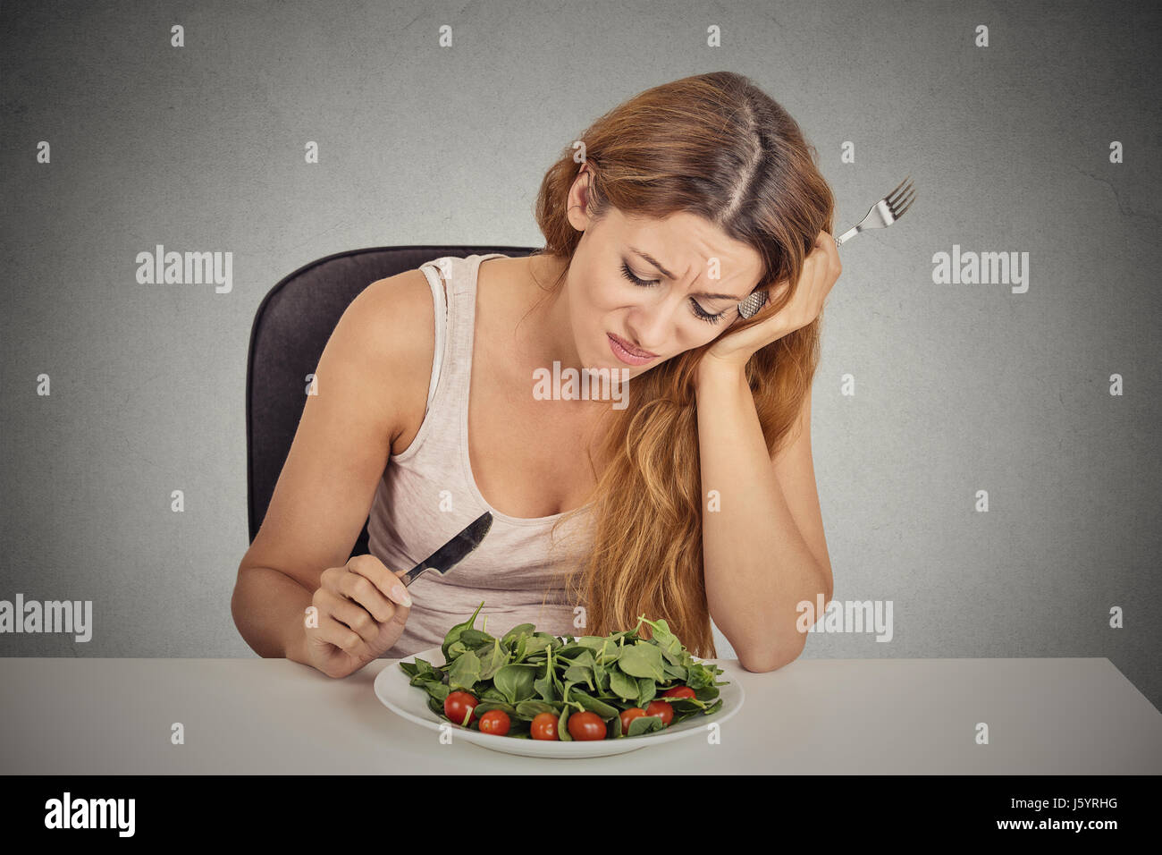 traurige unzufrieden junge Frau essen Salat isoliert graue Wand Background. Negativen menschliches Gesicht Ausdruck Emotion. Stockfoto