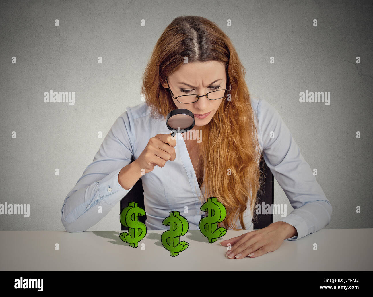 Pfennigfuchser. Geschäftsfrau, die Durchsicht Dollarzeichen Lupensymbol auf Tisch isoliert graue Wand Office-Hintergrund. Finanzielle Wirtschaft wir Stockfoto