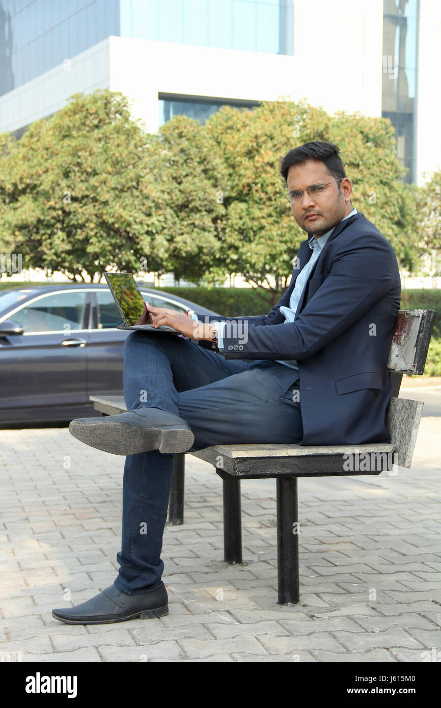 Junge indische Unternehmen Mann im Anzug sitzen auf Bank und arbeitet an seinem laptop Stockfoto