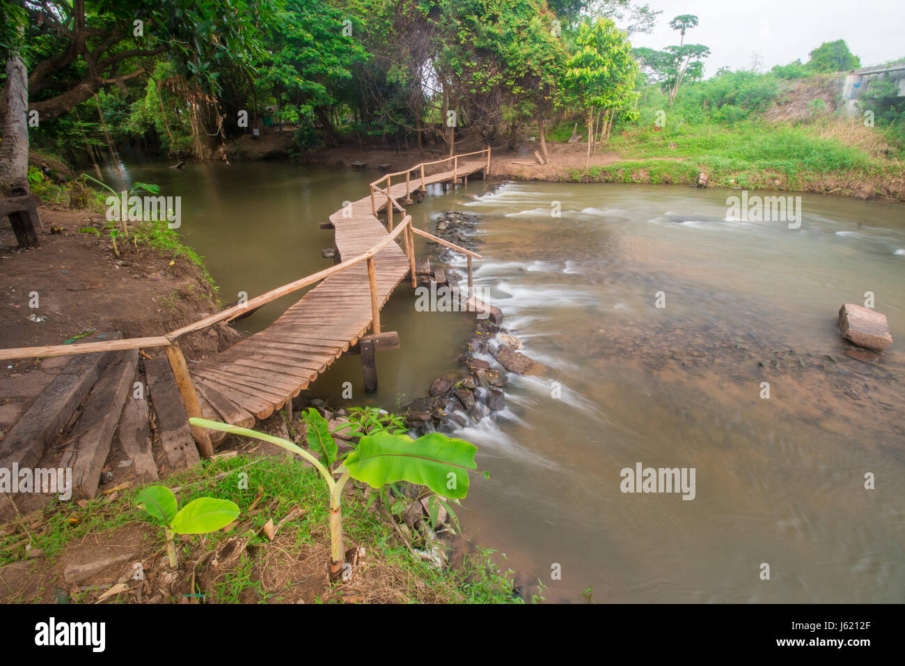 Eine hölzerne Brücke über den Fluss fließt in den Morgen. Stockfoto