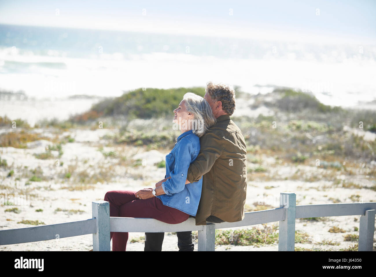 Liebevolle älteres Paar sitzt am Sonnenstrand Zaun Stockfoto