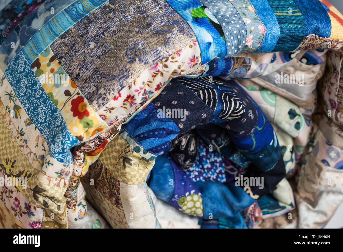 Nähen, Patchwork und Mode Konzept - Makro der leuchtend blaue schöne mehrfarbige gesteppte Decke zusammengerollt in der Röhre, Lager von fertigen Handarbeiten Produkten, Seitenansicht. Stockfoto