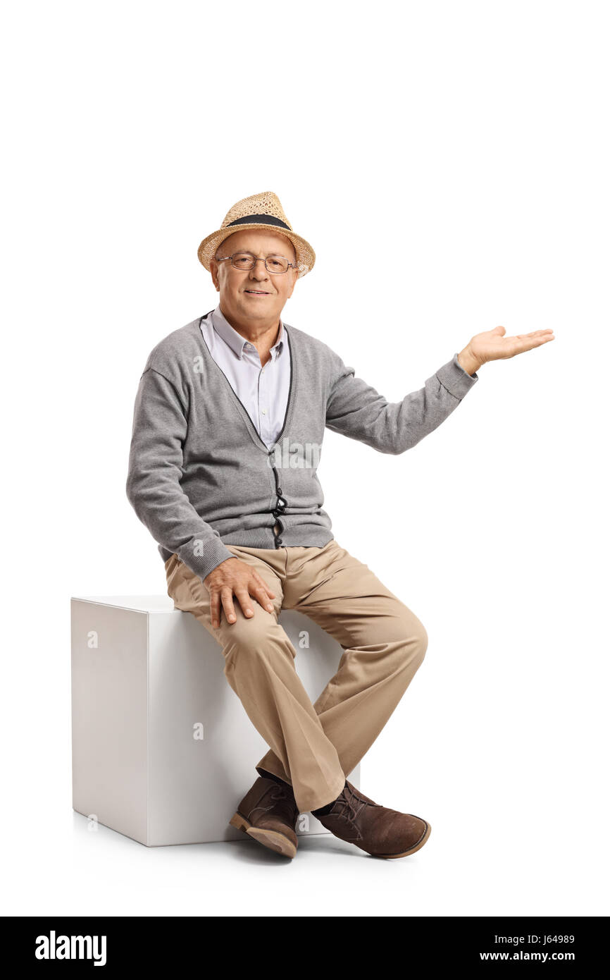 Senior sitzt auf einem Würfel und Gestikulieren mit seiner Hand isoliert auf weißem Hintergrund Stockfoto