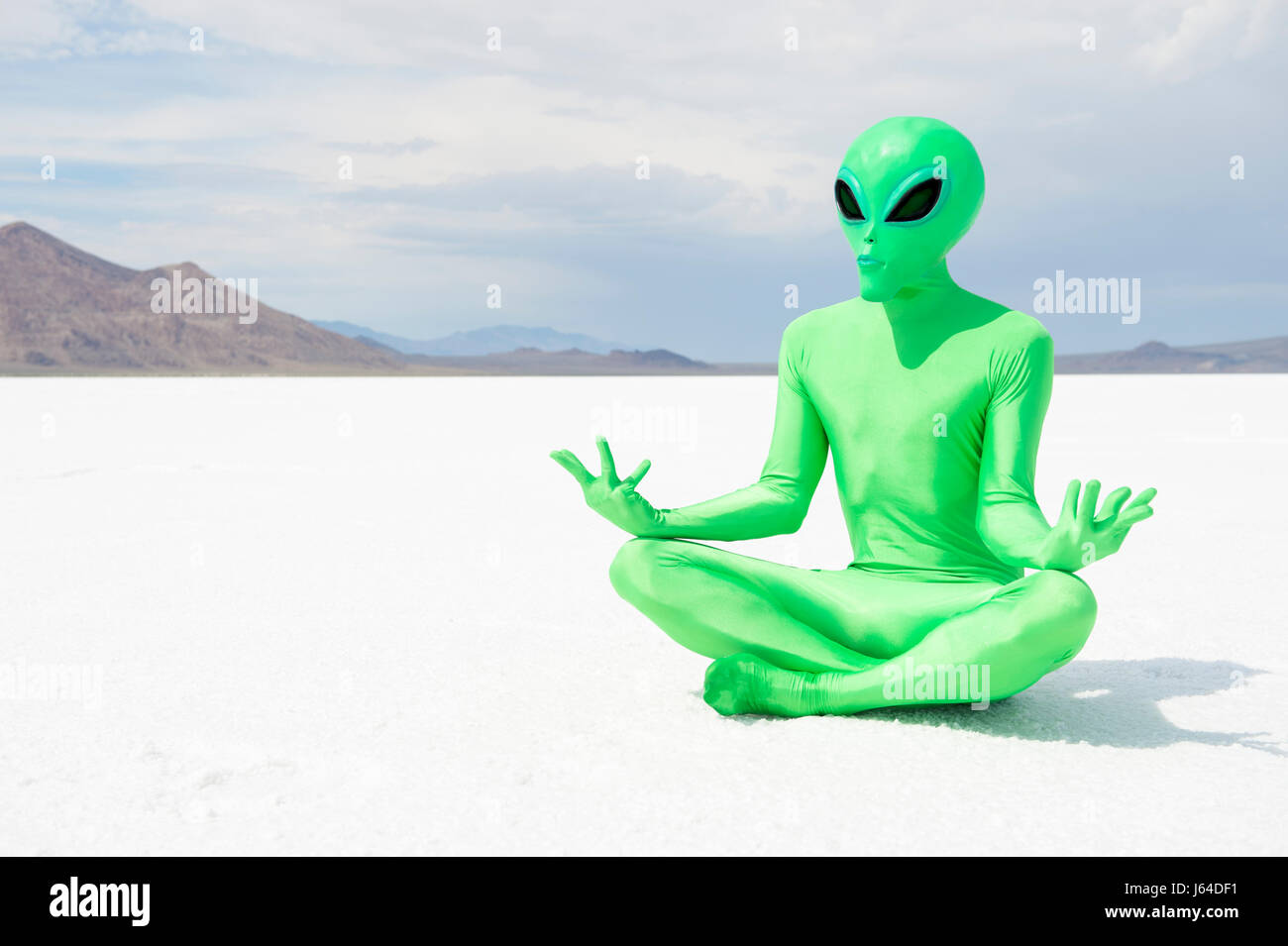 Grüne Alien üben transzendentale Meditation sitzen in einem Lotus-Position auf einer krassen jenseitigen Martian Wüstenlandschaft Stockfoto