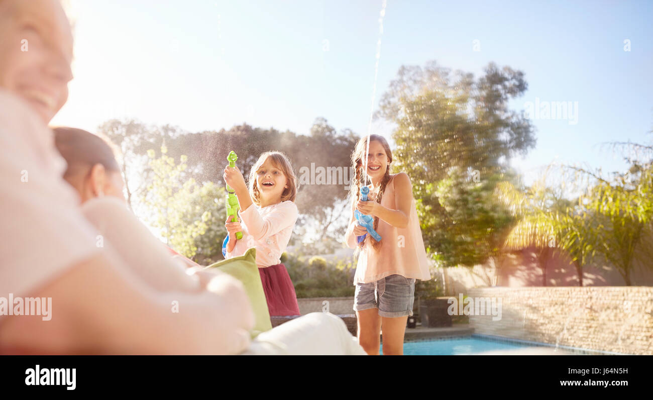 Verspielte Schwestern mit Spritzpistolen Besprühen mit Wasser am sonnigen Pool Stockfoto
