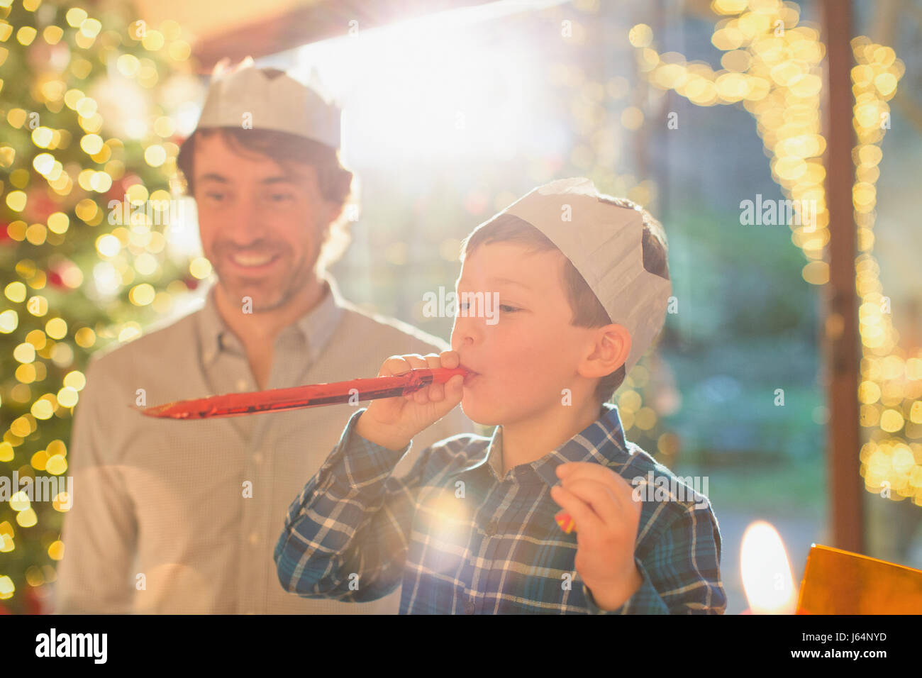 Vater und Sohn tragen Weihnachten Papier Kronen und bläst Parteibevorzugung Stockfoto