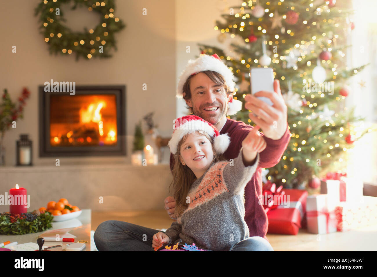 Vater und Tochter in Santa Hüte an Weihnachten Wohnzimmer Selfie mit Kamera-Handy Stockfoto