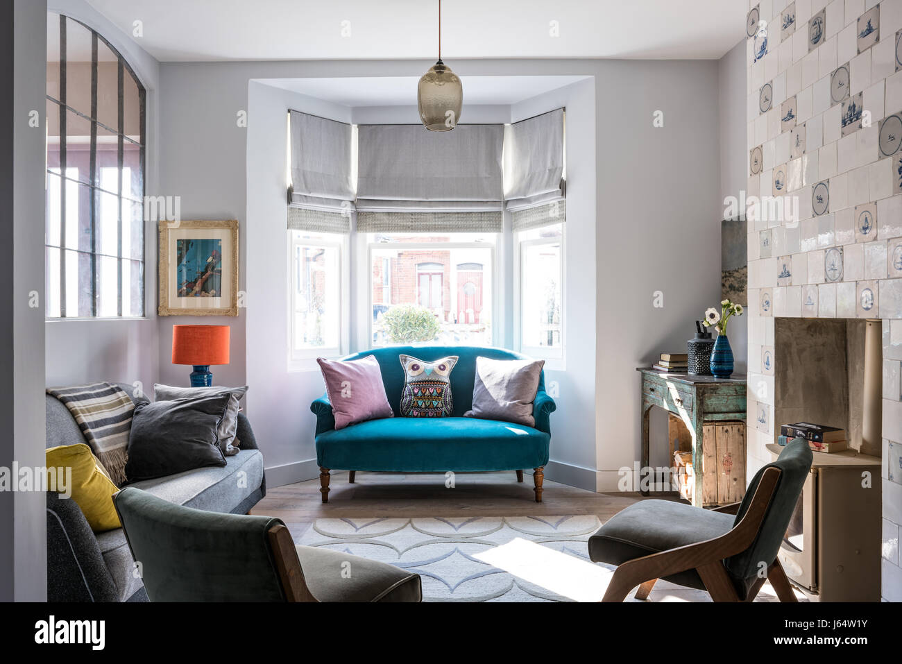 Große französische Metal geborgen Fenster im Wohnzimmer mit Delfter Kacheln Kamin. Das graue Vintage Sofa ist aus Französisch-Affäre. der Teppich von Allegra Stockfoto