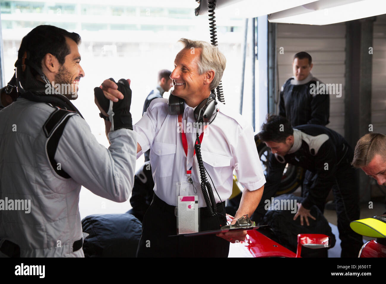 Manager und Formel 1-Fahrer feiern, Handshaking in Werkstatt Stockfoto
