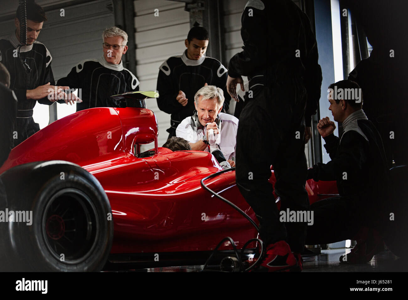 Manager und Pit Crew arbeiten an der Formel 1 Rennwagen in dunklen Werkstatt Stockfoto