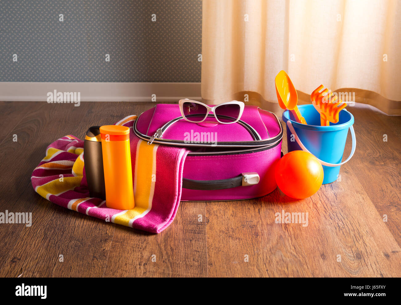 Rosa Tasche, Sonnenbrillen, Handtuch, Sonnencreme und Strand Plastikspielzeug auf Parkettboden. Stockfoto