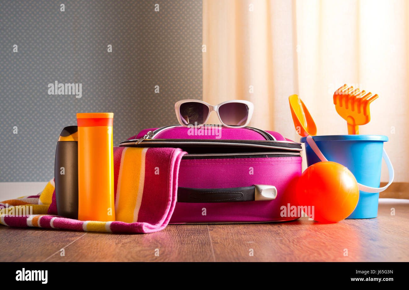 Rosa Tasche, Sonnenbrillen, Handtuch, Sonnencreme und Strand Plastikspielzeug auf Parkettboden. Stockfoto
