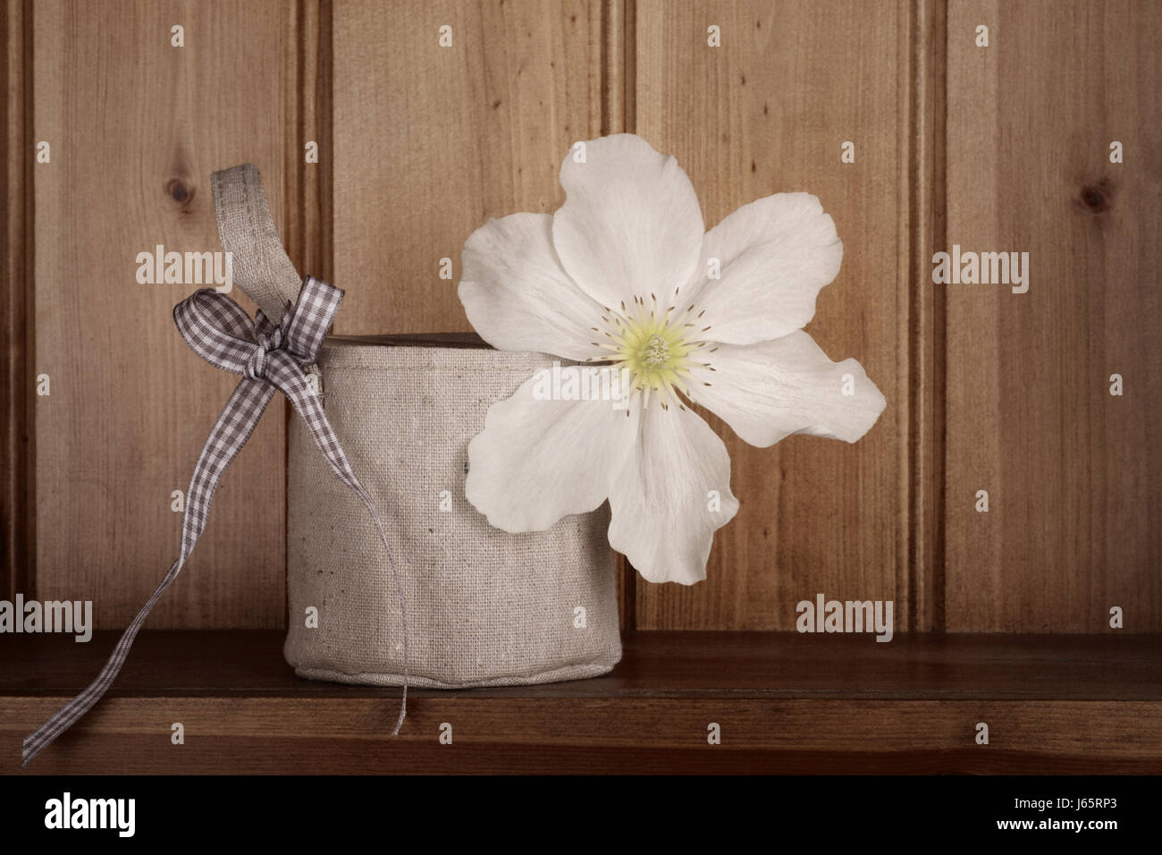 Atemberaubende weiße Clematis in einer Vase, bedeckt von einer hessischen Tasche mit karierte Schleife zu handhaben. Entsättigung Land rustikale Wirkung beantragt. Stockfoto