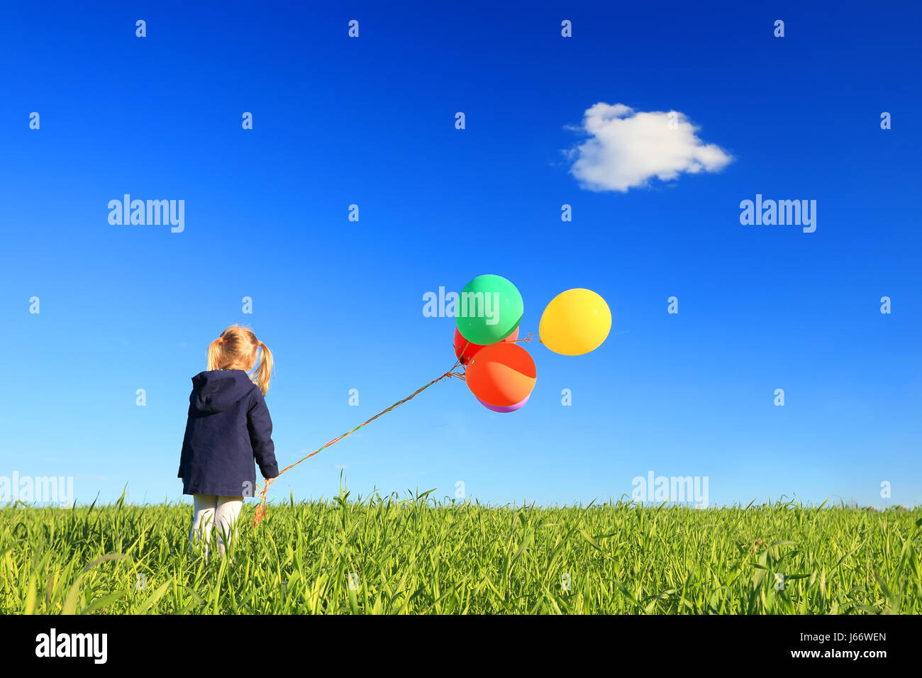 Kleines Mädchen mit Luftballons in grüne Wiese. Kind auf blauen Himmelshintergrund. Blauer Himmel mit einer Wolke über kleine Mädchen mit bunten Luftballons. Kind Stockfoto