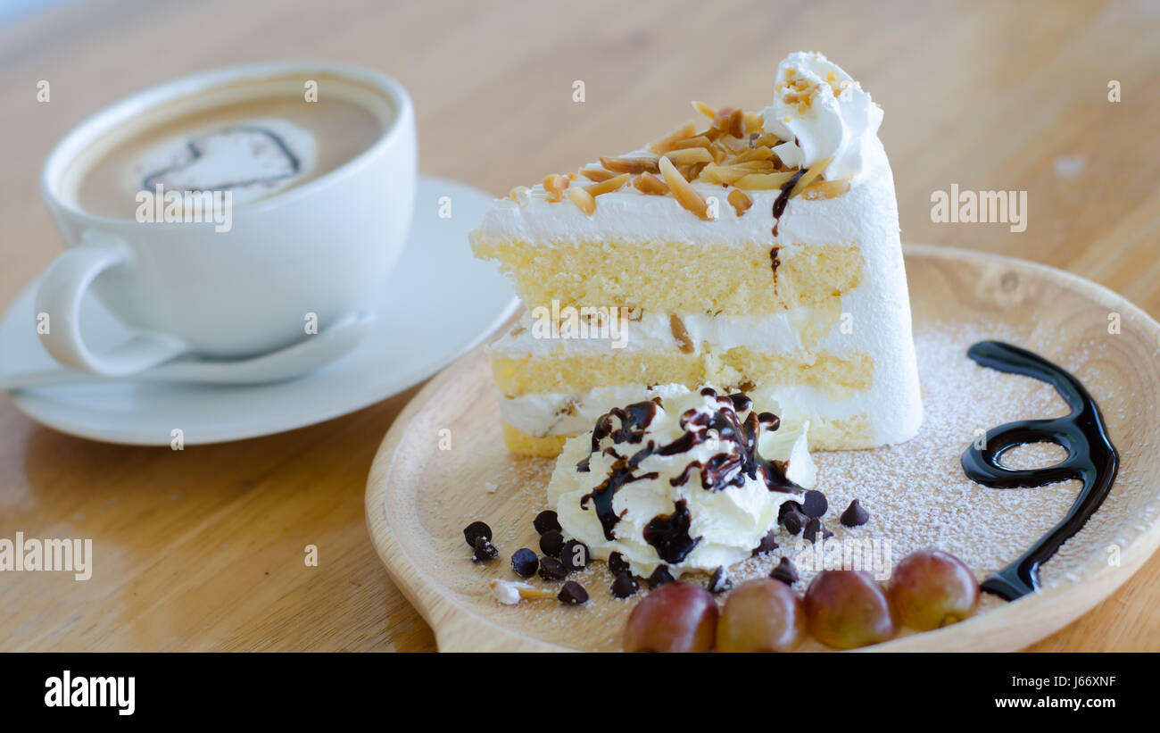 Nahaufnahme Mandel Kuchen und Kaffee Tasse mit Herz Form Latte Art auf Holztisch Stockfoto