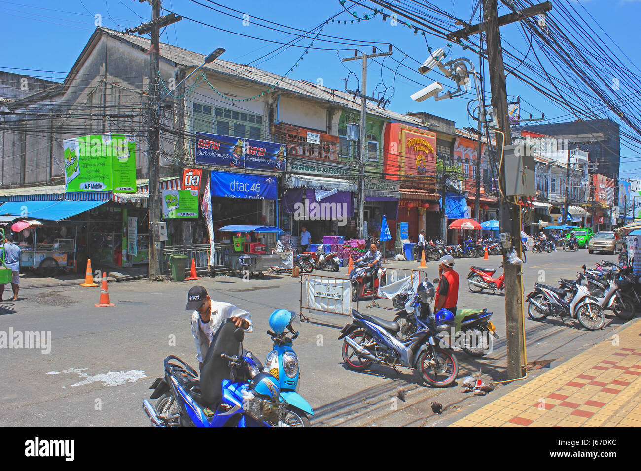 Straße in der Altstadt von Phuket mit bunten Geschäften und anzeigen, öffnen Sie elektrische Netze und Männer mit ihren Motorrädern. Stockfoto