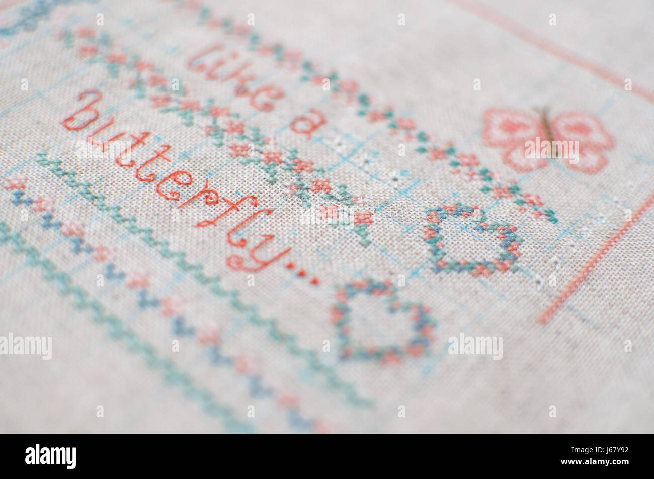 Kreuzstich-Stickerei auf Leinen. Sampler mit floralen Mustern, Herz und Schmetterling. Hautnah. Selektiven Fokus. Stockfoto