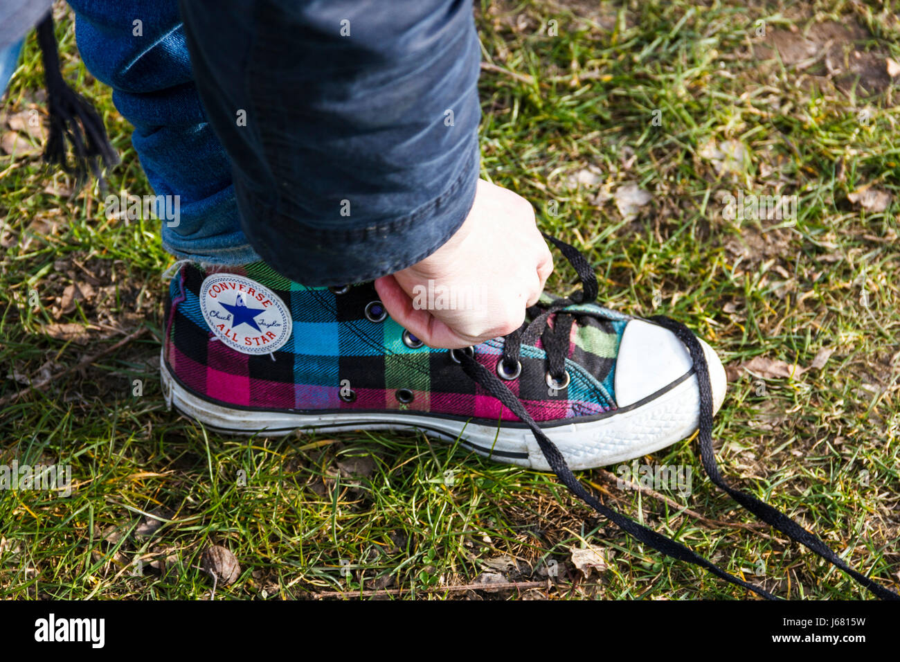 Erwachsene Person binden eine rückgängig gemachte Schuhbändern auf einem Tartan-gemusterten Converse All Star' Schuh Stockfoto