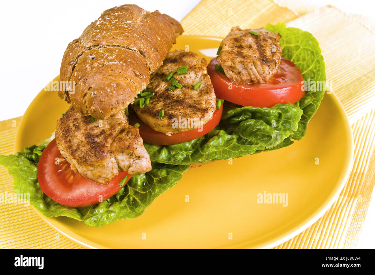 Belegtes Vollkorn Brötchen mit Schweinefleisch, Salat, Tomaten und Paprika auf gelb Stockfoto