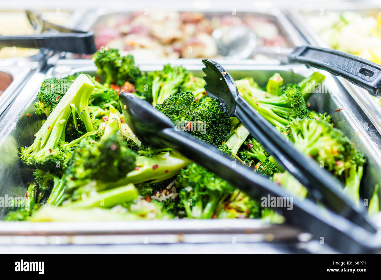 Makro Nahaufnahme von gedämpften Brokkoli mit Paprikaflocken in Buffetform mit einer Zange Stockfoto