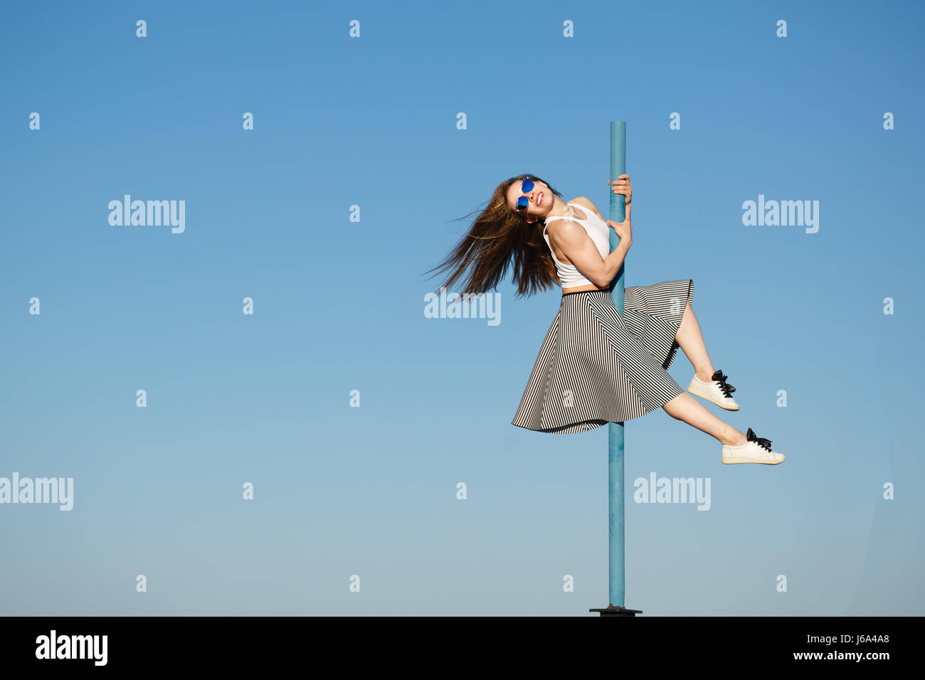 Junge attraktive Mädchen Hipster tanzen auf der Pole. Sie ist in einem Oberteil, Rock und Sonnenbrille bekleidet. Fliegende Haare. Das Konzept des Lebens in Bewegung. Stockfoto