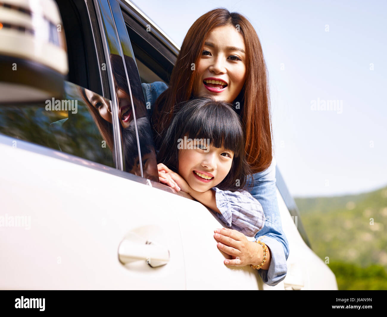 junge asiatische Mutter und Tochter während der Fahrt in einem Auto Heckscheibe ihre Köpfe herausragen. Stockfoto