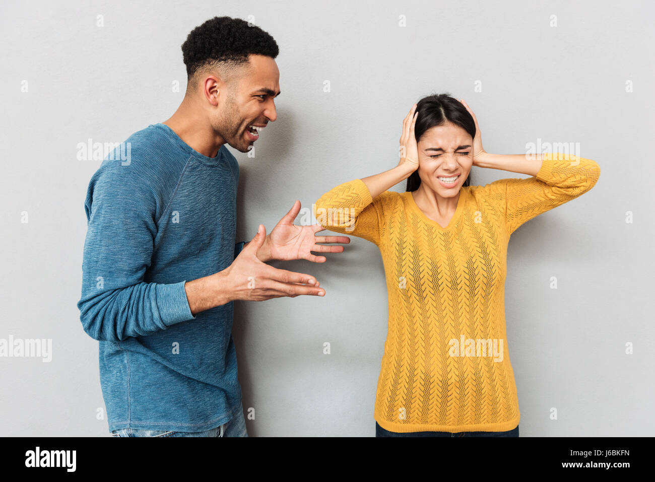 Afrikanischen aggressiven Mann schreien an seine Frau während sie schließen Ohren über grauen Hintergrund isoliert Stockfoto