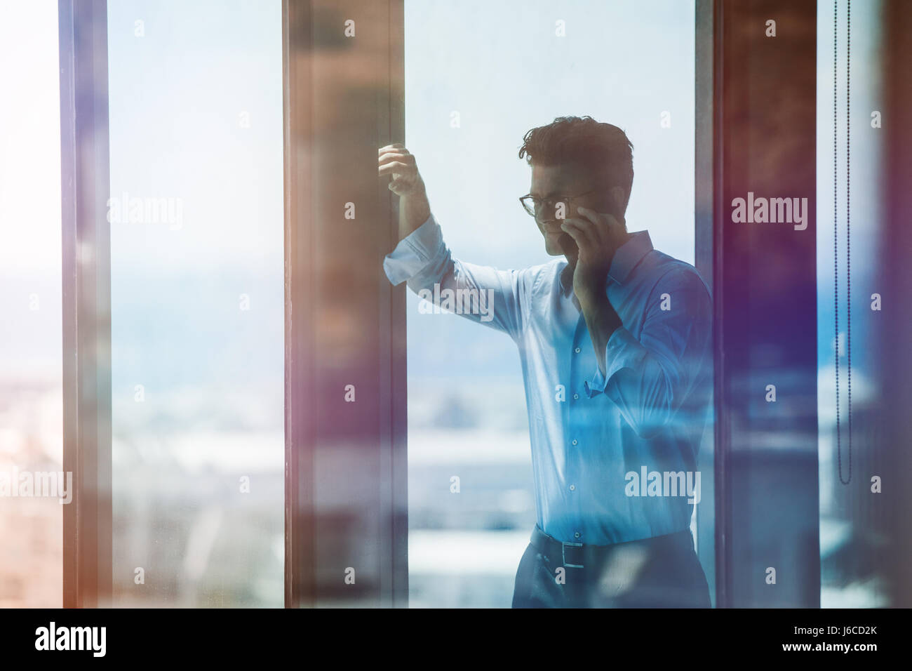Glücklich Kaufmann Fenster stand und reden über Handy. Männliche Führungskraft in Bürogebäude und Mobiltelefon zu benutzen. Stockfoto
