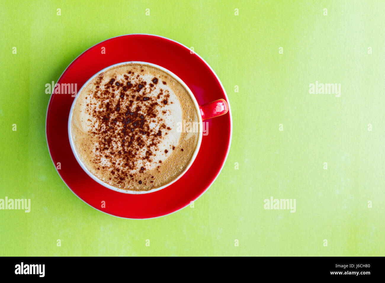 Blick von oben auf einer schaumigen Tasse Cappuccino Kaffee in eine rote Tasse und Untertasse und auf eine bunte, grüne Fläche. Stockfoto