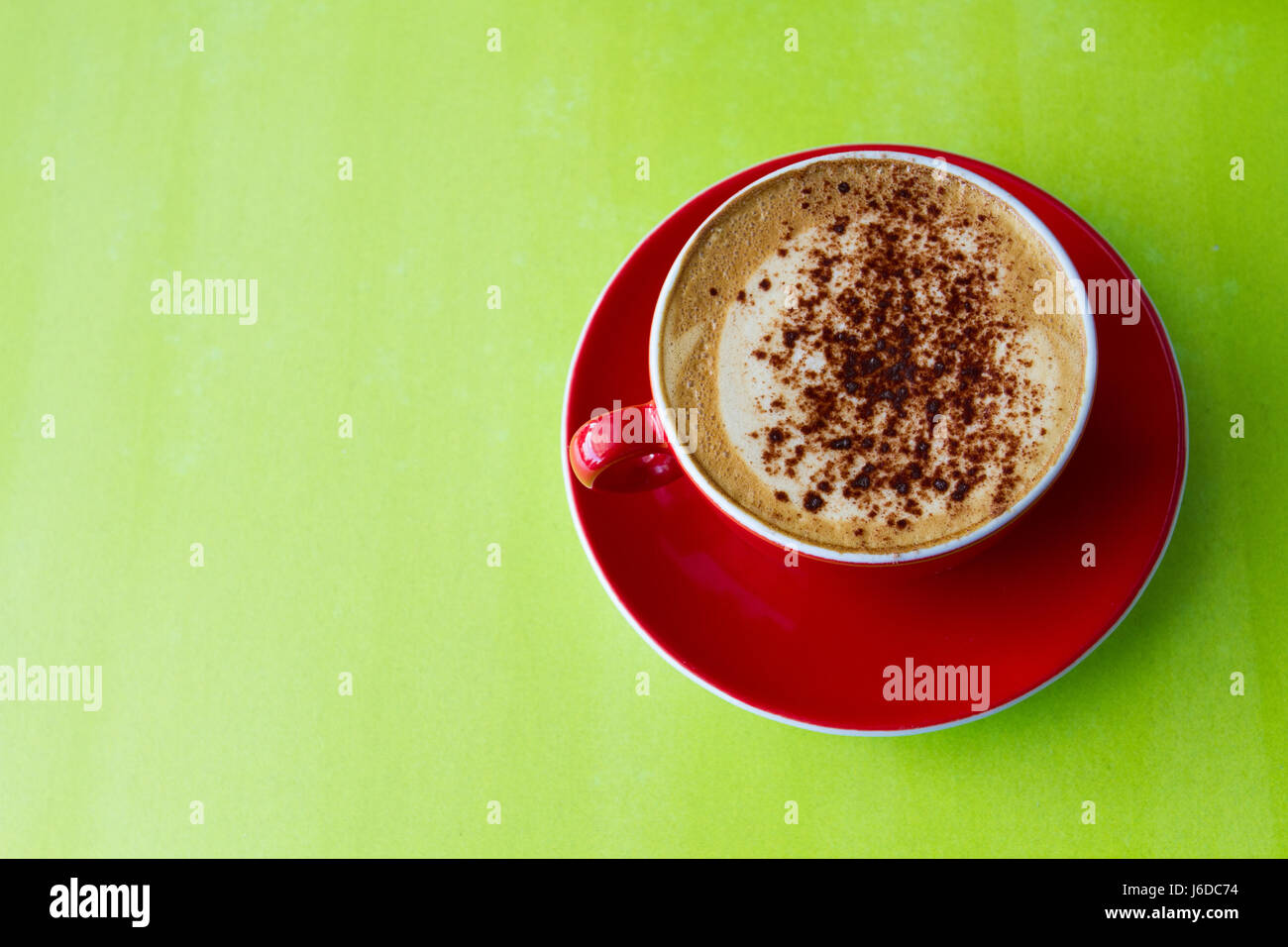 Blick von oben auf einer schaumigen Tasse Cappuccino Kaffee in eine rote Tasse und Untertasse und auf eine bunte, grüne Fläche. Stockfoto