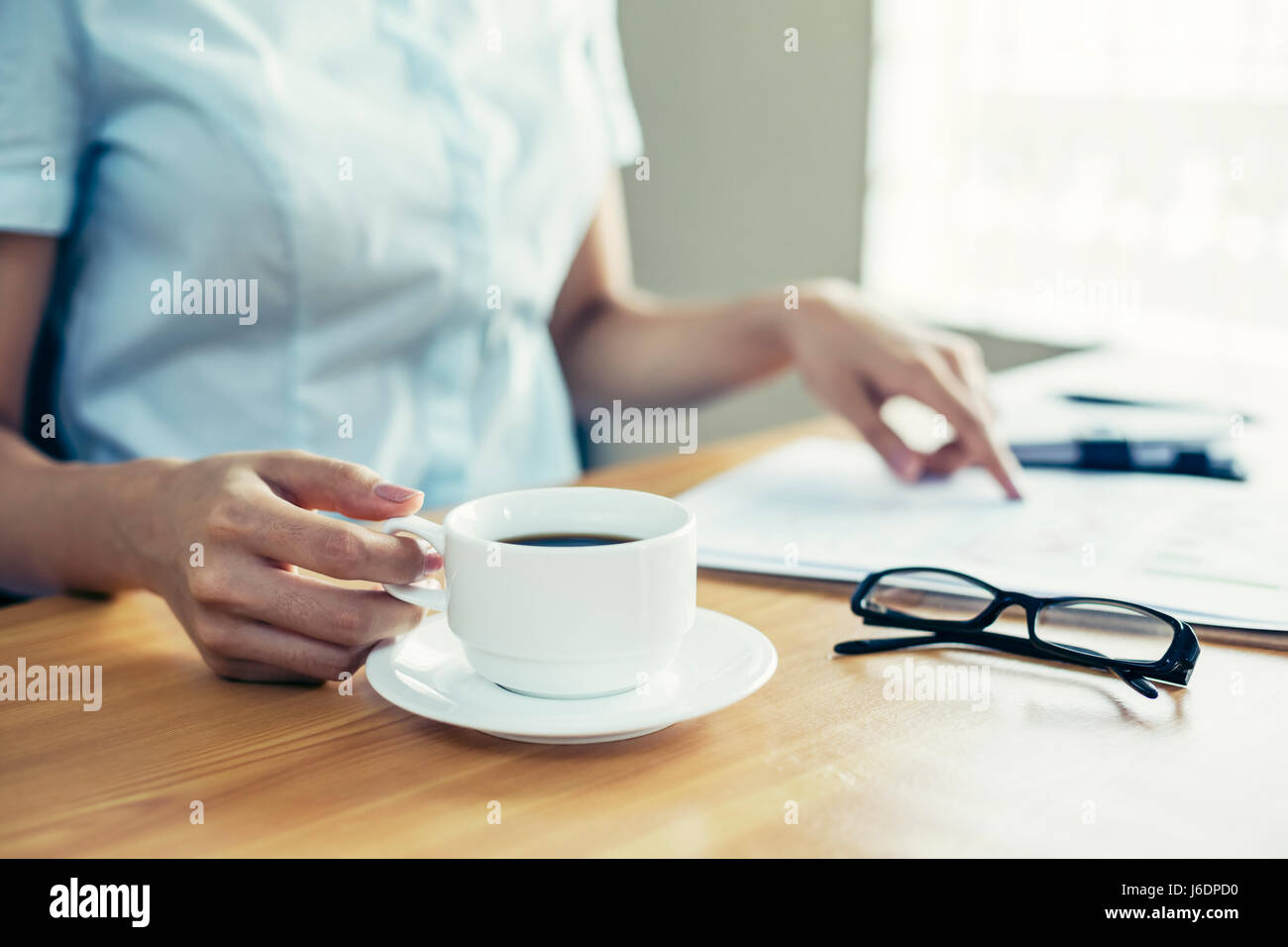 Geschäftsfrau indoor lesen Dokument auf ihrem Schreibtisch und hält Kaffee cub Stockfoto