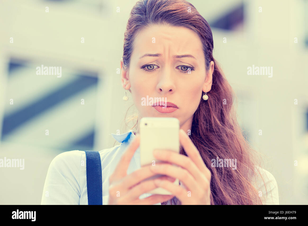 Verärgert gestresst Frau mit Handy angewidert mit Meldung, dass sie isoliert Firmengebäude Hintergrund erhalten. Sad suchen menschliches Gesicht Ausdruck e Stockfoto