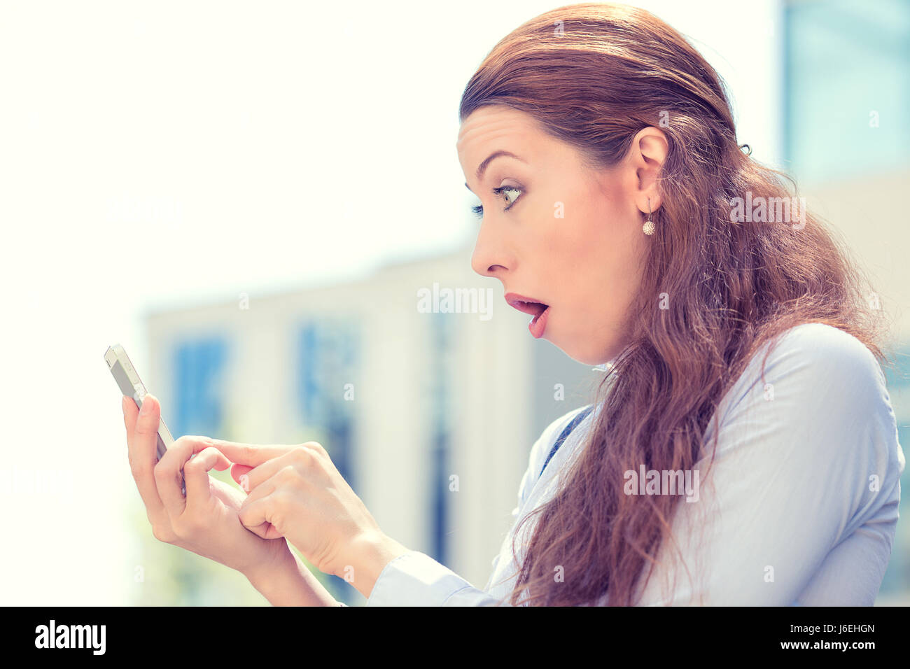 Seite Profil Closeup Portrait ängstliches junge Mädchen auf der Suche am Telefon sehen, schlechte Nachrichten oder Fotos mit ekelhaft Emotion im Gesicht isoliert außerhalb der Stadt Stockfoto