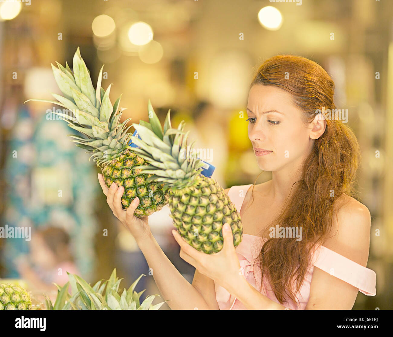 Attraktive Frau im Supermarkt einkaufen. Closeup Portrait schöne junge Frau abholen, die Auswahl der Früchte, Ananas im Lebensmittelgeschäft. Positive fa Stockfoto