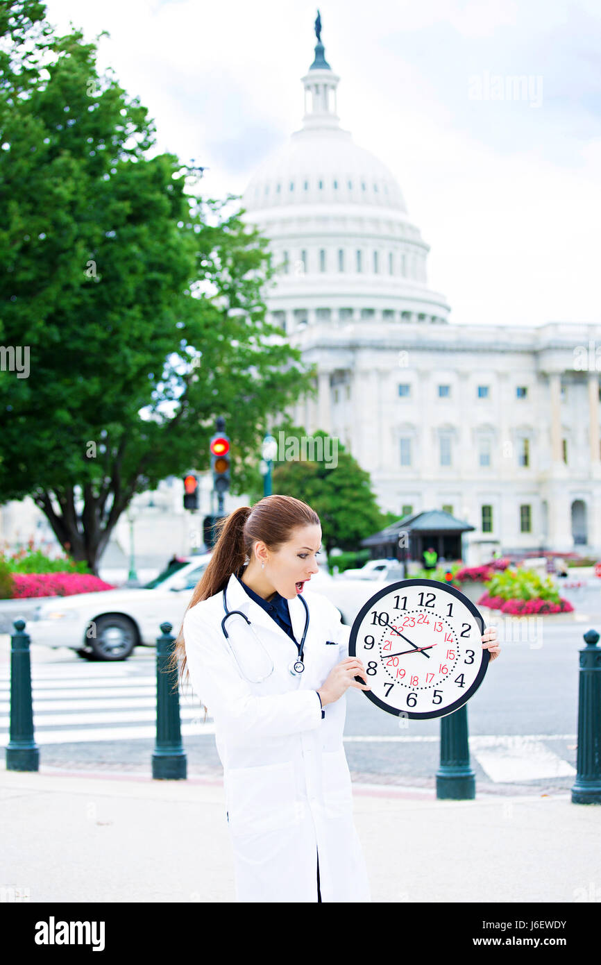 Closeup Portrait, überwältigt, beschäftigt, unglücklich betont weibliche Ärztin, Frau Doktor hält Wanduhr auf Straßen Washington DC, runni Stockfoto