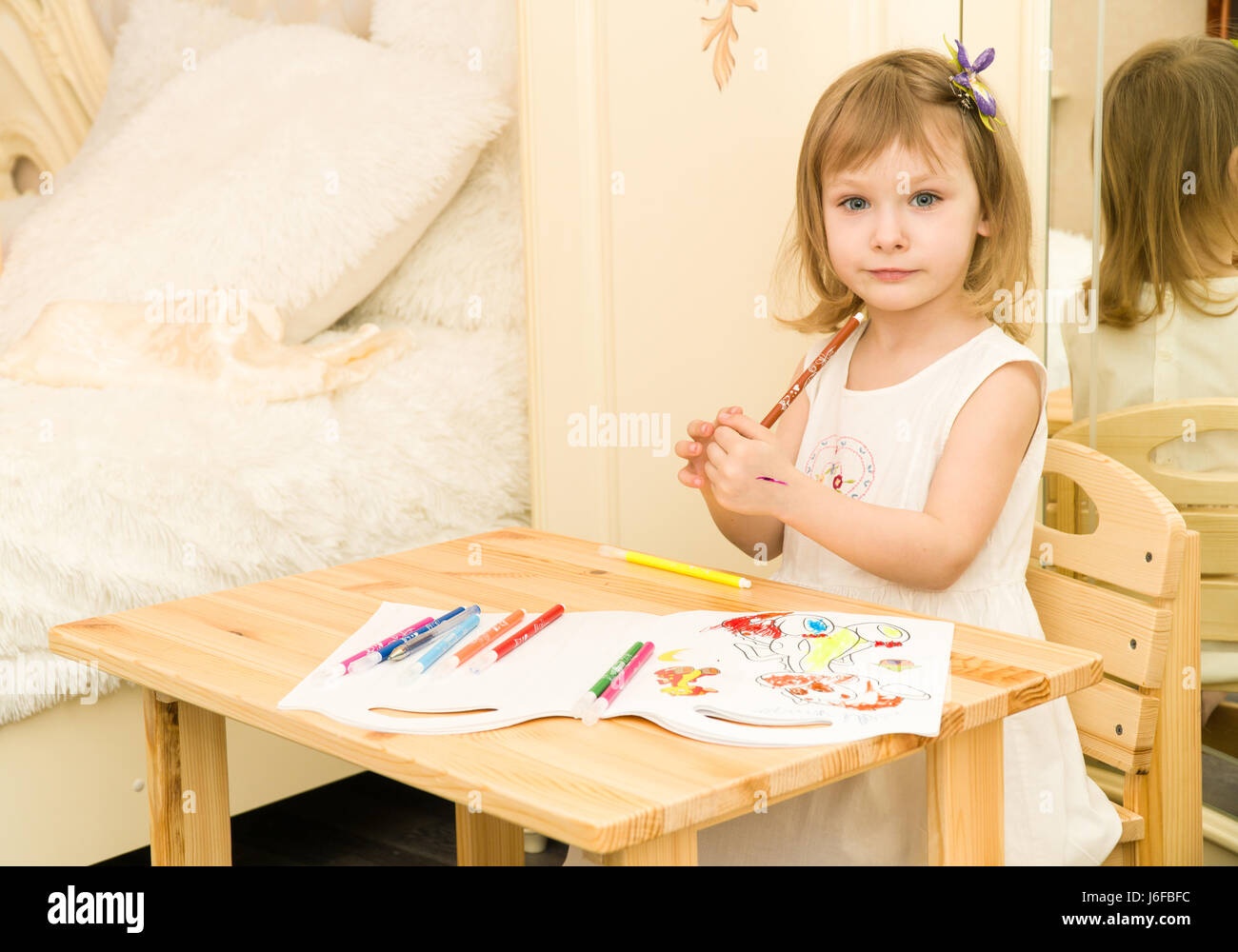 Aktiv im Vorschulalter Kindlein, niedlichen Kleinkind Mädchen mit blonden lockigen Haaren, Zeichnung Bild auf Papier mit bunten Stiften und Filzstifte, sitzt am Tisch aus Holz im Innenbereich zu Hause oder im kindergarten Stockfoto