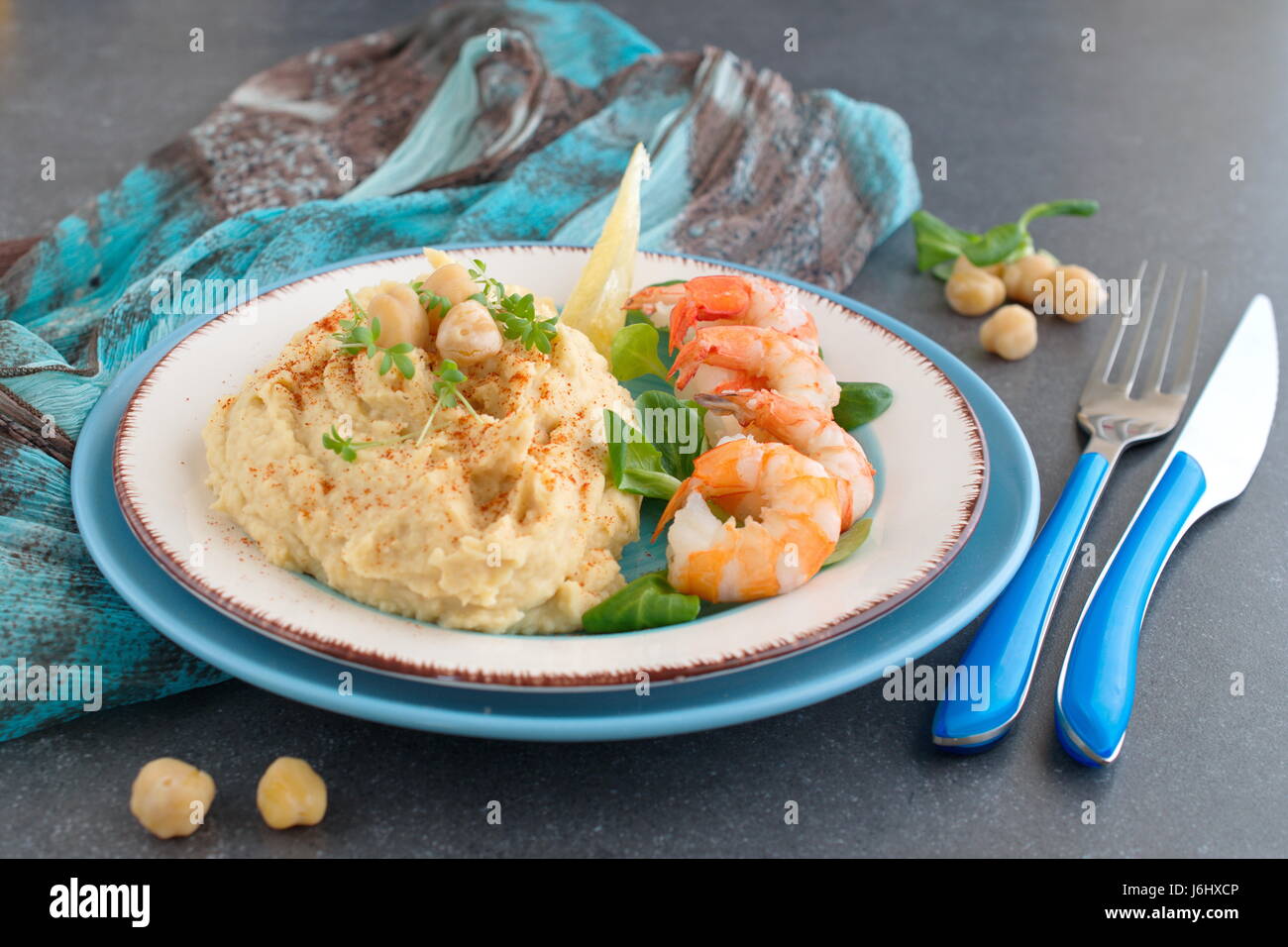Kichererbsen-Püree mit Sahne und Butter serviert mit gekochten Garnelen auf einer weißen und blauen Platte auf einem grauen abstrakten Hintergrund. Gesunde Ernährung. Gesunde Ernährung-Konzept. Stockfoto