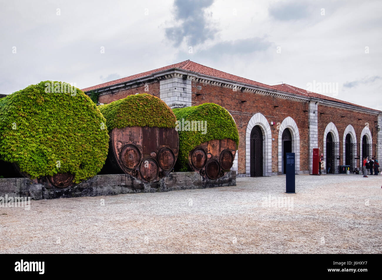 Hafen von Venedig, Castello, Arsenale. Industrielle rostigen alten Eisen Fass Behälter abgedeckt Efeu neben historischen alten Backsteingebäude Gehäuse Biennale Stockfoto