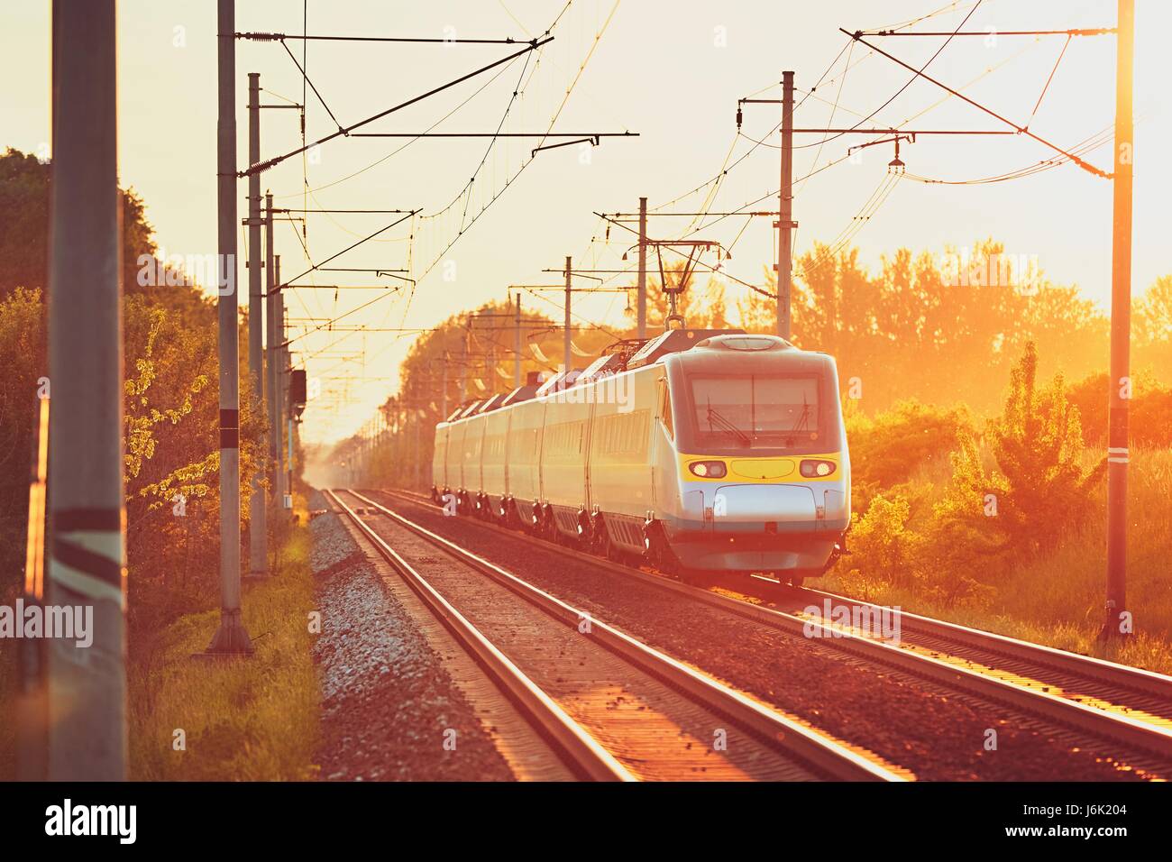 Reisen mit modernen Personenzug. Bahn auf den wunderschönen Sonnenuntergang (Goldene Stunde). Stockfoto