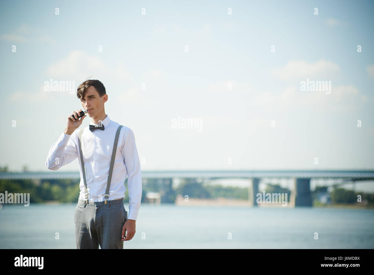 junge magerer Mann, elegant stilvoll gekleidet in weißem Hemd, Hose mit Hosenträgern und Fliege. Vaper Kerl raucht eine e-Zigarette, Releas Dämpfe Stockfoto