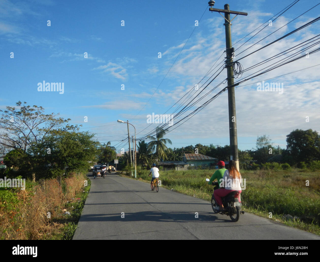 Dies bezieht sich auf ein ländliches Gebiet in Baliuag, Bulacan, mit Reisfeldern, Grasland, Bäumen, Häuser und ein Bewässerungssystem. Die Straße und die Brücken deuten auf eine wichtige Infrastruktur in der Region hin, die das landwirtschaftliche Leben unterstützt. Stockfoto
