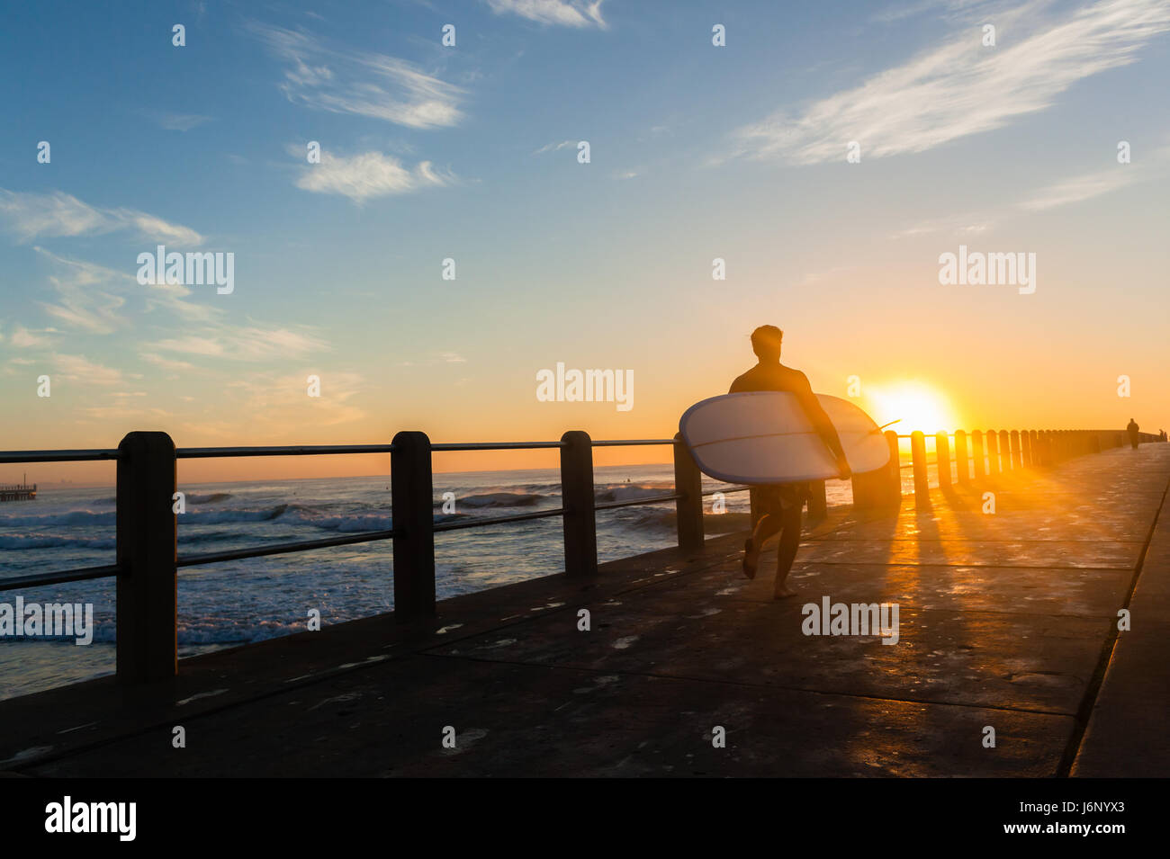 Surfer mit Longboard ausgeführte Strand Ozean Pier Silhouette Dawn Sonnenaufgang. Stockfoto