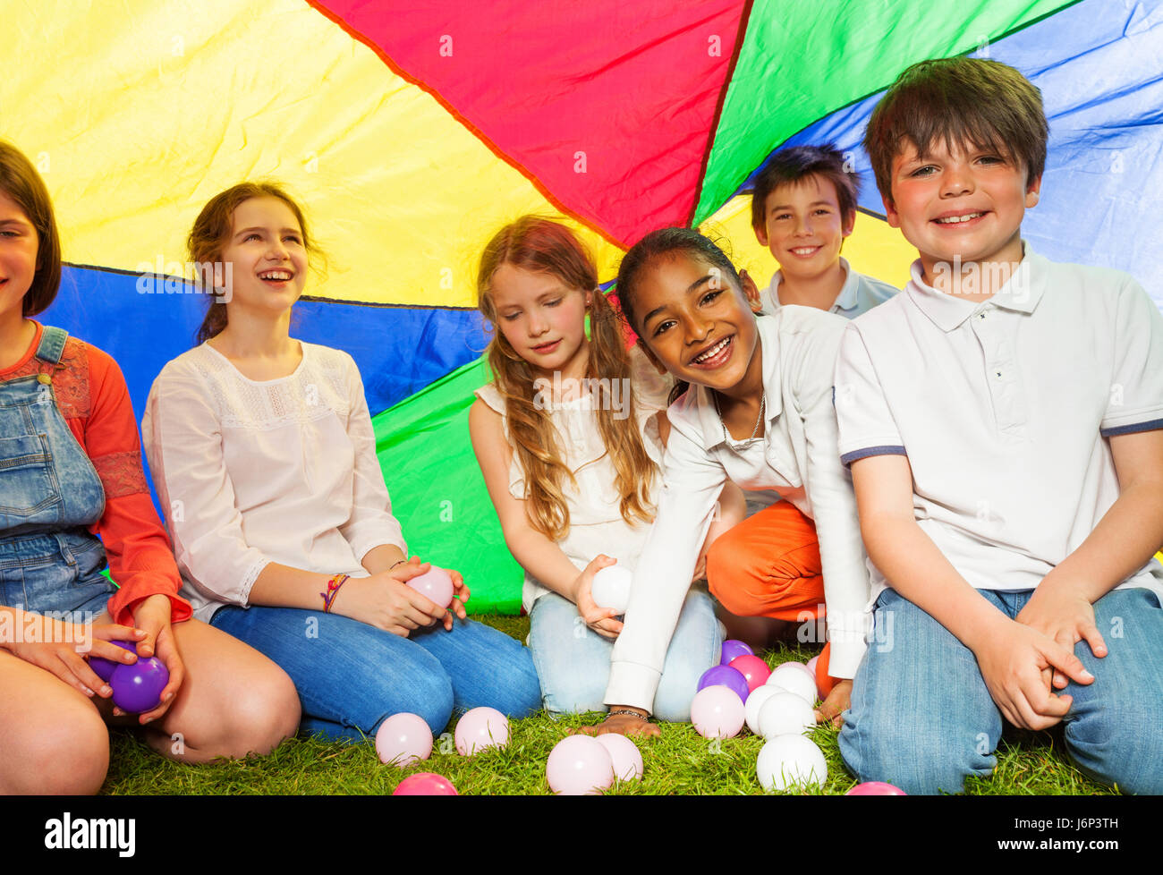 Große Gruppe von sechs glückliche Kinder, 10-12 Jahre alten Jungen und Mädchen gemacht sitzen unter Vordach des Regenbogen-Fallschirm Stockfoto