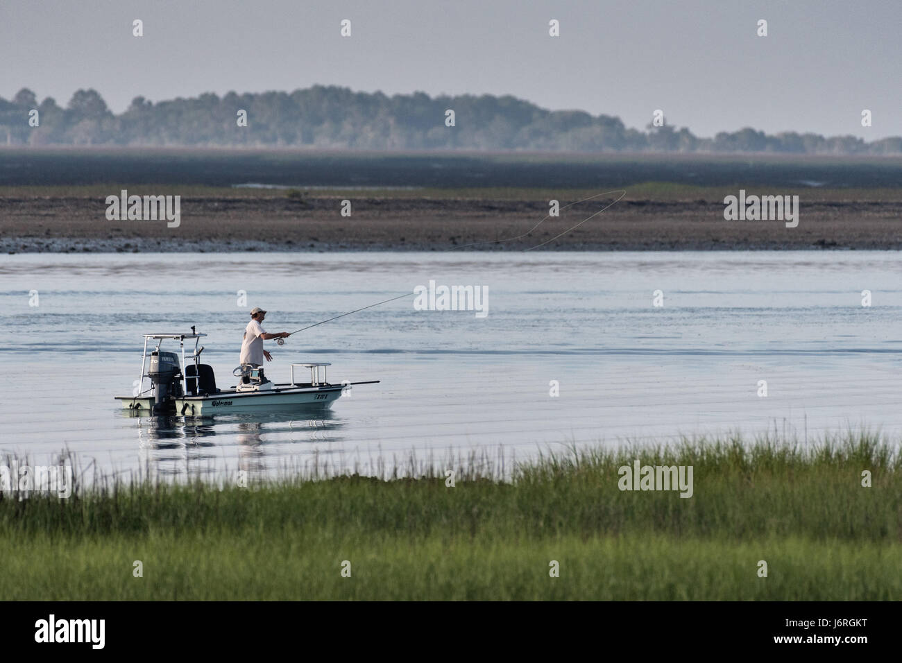 Eine wohnungen Fischer wirft eine Fliegenrute von einem kleinen Boot in den Salzwiesen der Kap Romain National Wildlife Refuge in der Nähe von Charleston, South Carolina. Die 66,287 Hektar National Wildlife Refuge umfassen Wasser Aufstauungen, Buchten, Buchten, emergent Salzwiesen und Barriere Inseln, von denen die meisten ist nur mit dem Boot erreichbar. Stockfoto