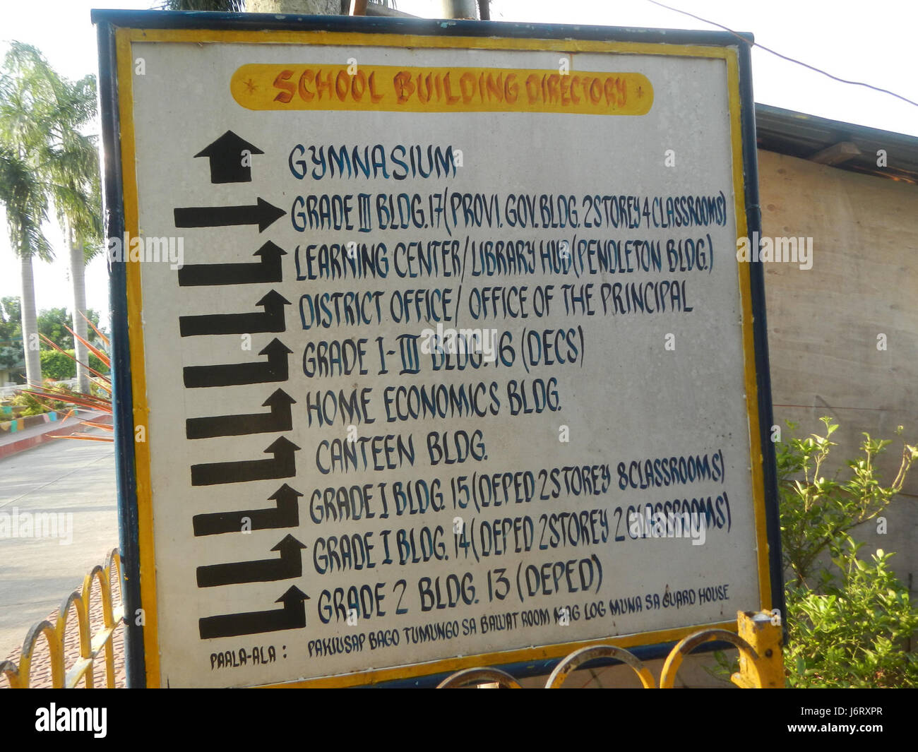Dieses Bild zeigt die Pulilan Central School in Bulacan, mit einem Schwerpunkt auf der Champagnerpalme und dem nahegelegenen Fluss, die als natürliche Wahrzeichen in der Gegend dienen. Stockfoto