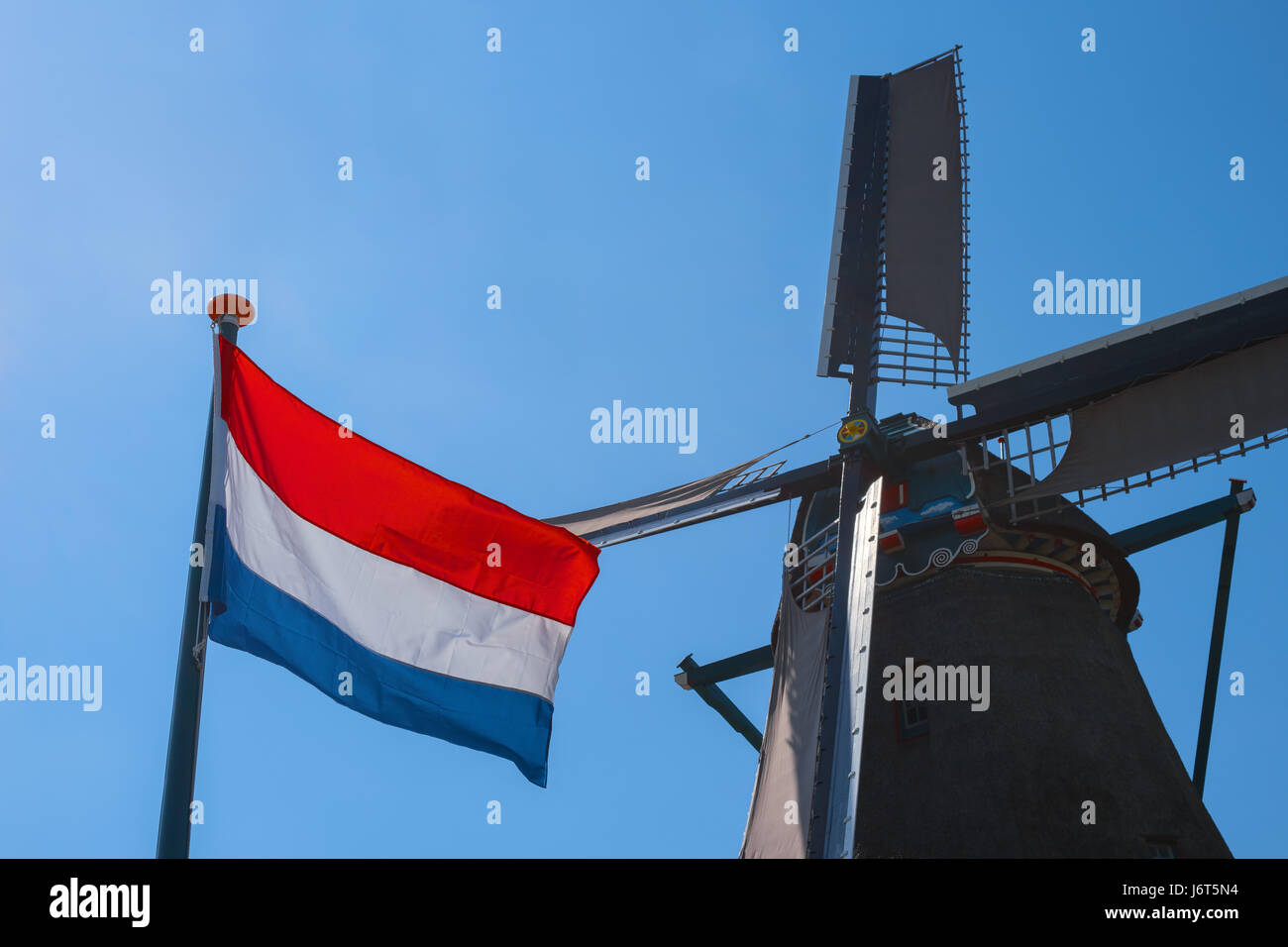 Berühmte alte holländische Windmühle und Flagge der Niederlande, Zaanse Schans, Niederlande, Europa. Typische holländische Mühle. Ländliche Landschaft in Holland. Symbol der t Stockfoto