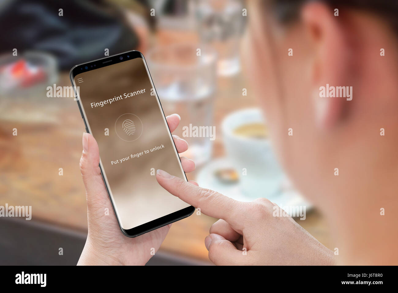 Frau verwenden Fingerabdruck Sicherheits-app für Handy und Datensicherheit. Modernes Mobiltelefon mit abgerundeten Ecken. Kaffee am Tisch im Hintergrund. Stockfoto