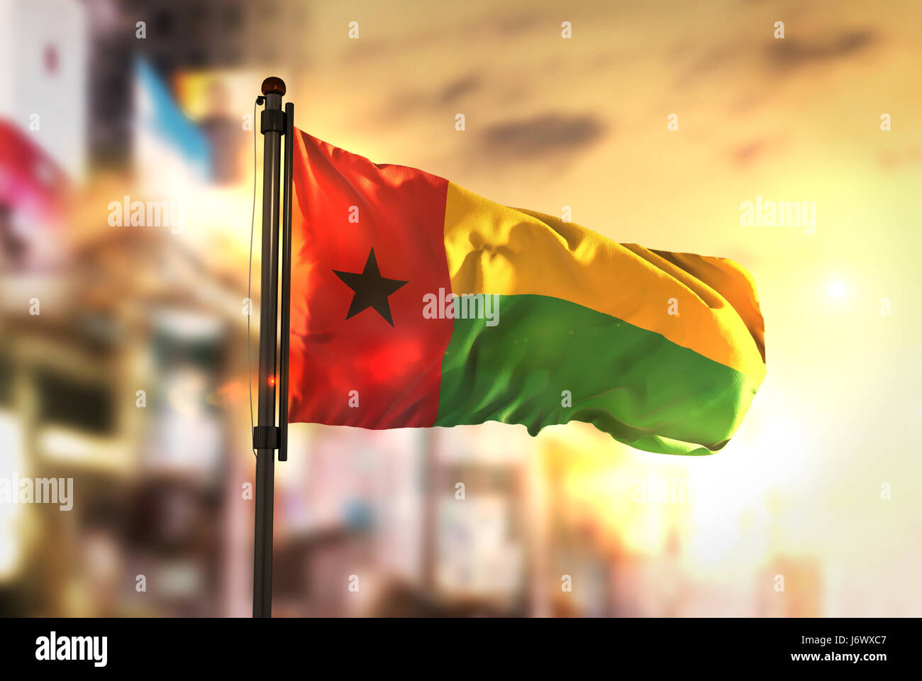 Guinea-Bissau-Flagge gegen City unscharf Hintergrund bei Sonnenaufgang Hintergrundbeleuchtung Stockfoto