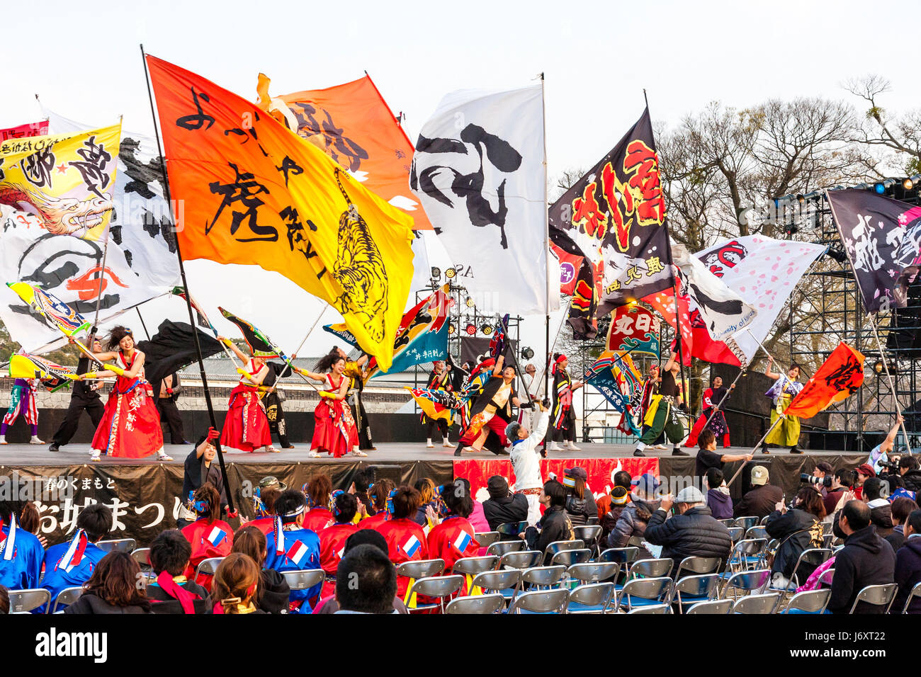 Yosakoi Tänzer in Rot und Weiß Kostüme, Tanz auf der Bühne, während wirbelnden riesige bunte Fahnen vor Publikum in Kumamoto, Japan. Stockfoto