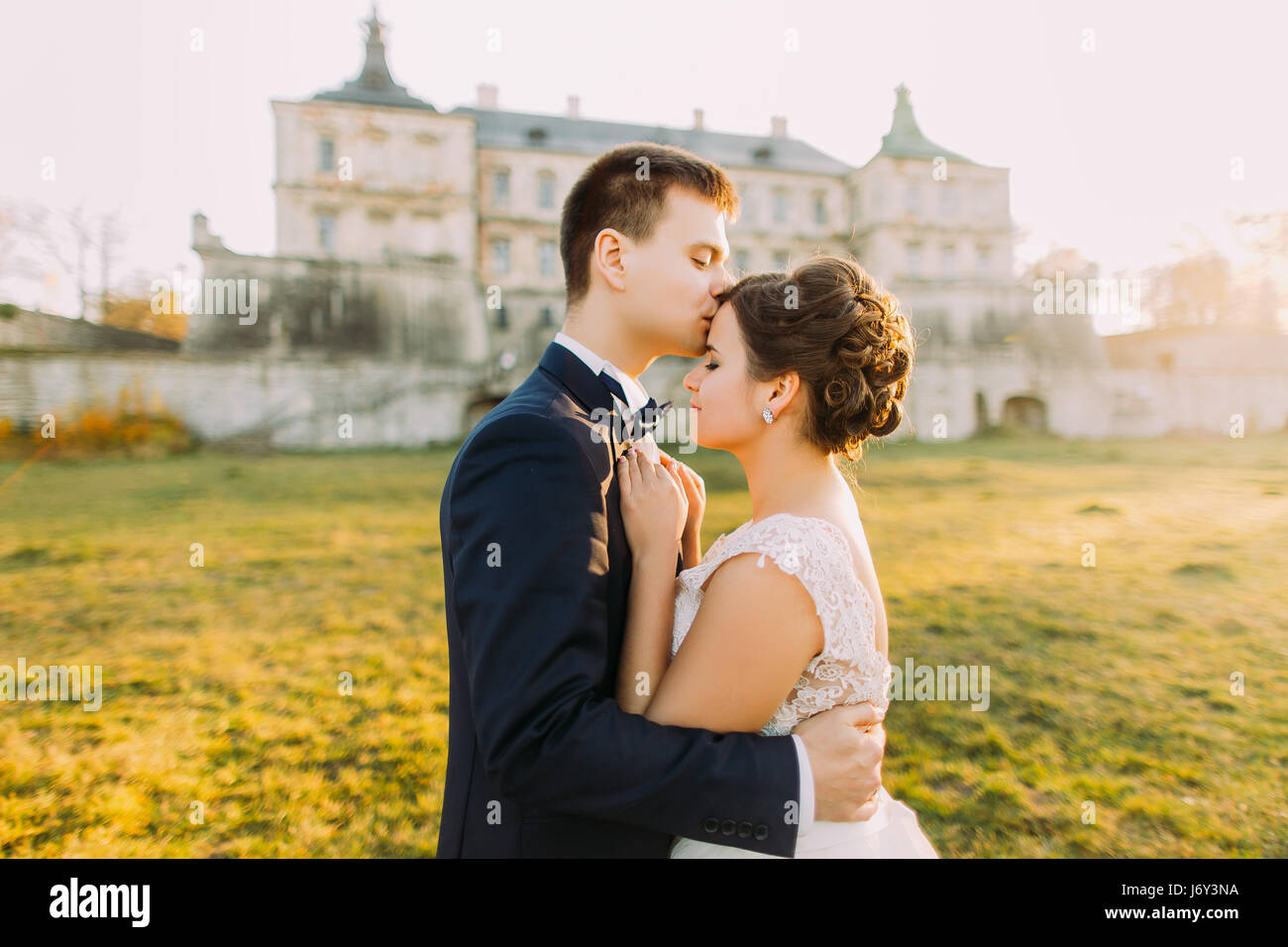 Der Bräutigam ist die schöne Braut in der Stirn auf den Hintergrund der alten gotischen Burg küssen. während des Sonnenuntergangs. Detailansicht Stockfoto